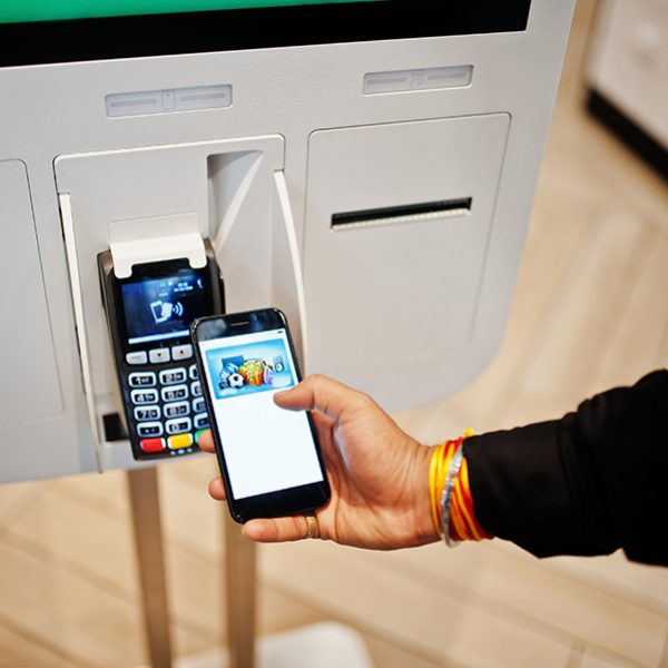 Hands of man customer at store place orders and pay by contactless credit card on mobile phone through self pay floor kiosk for fast food, payment terminal. Pay pass.