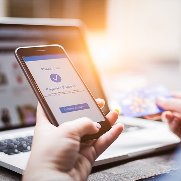 Online shopping concept, young woman hands holding mobile phone showing payment success information on screen with credit card and laptop computer on table while relax at home